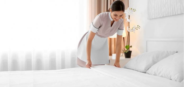 Young maid making bed in light hotel room